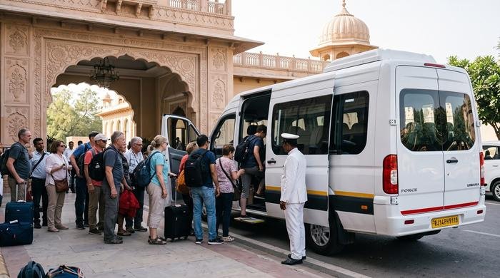 Group of tourists boarding a white Force Urbania van at a Jaipur palace with a chauffeur assisting